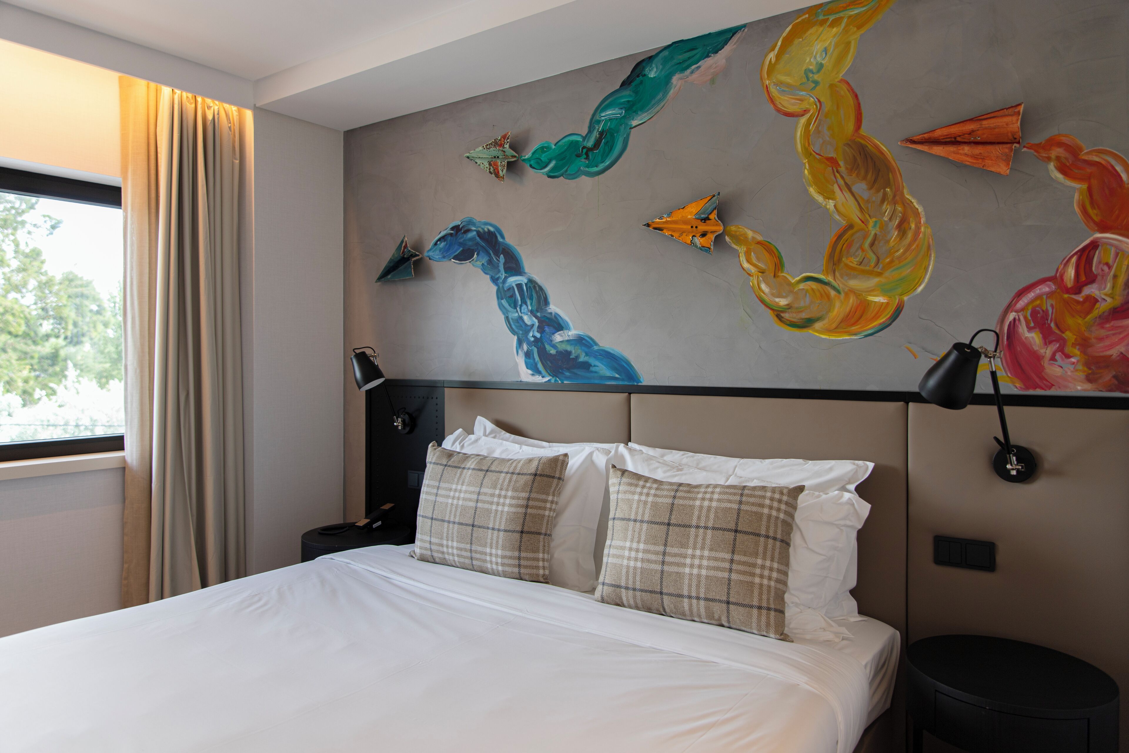 Habitación de hotel con cama, mesita de noche, lámpara y una pared decorada con arte abstracto.