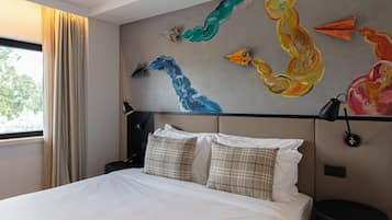 Habitación de hotel con cama, mesita de noche, lámpara y una pared decorada con arte abstracto.