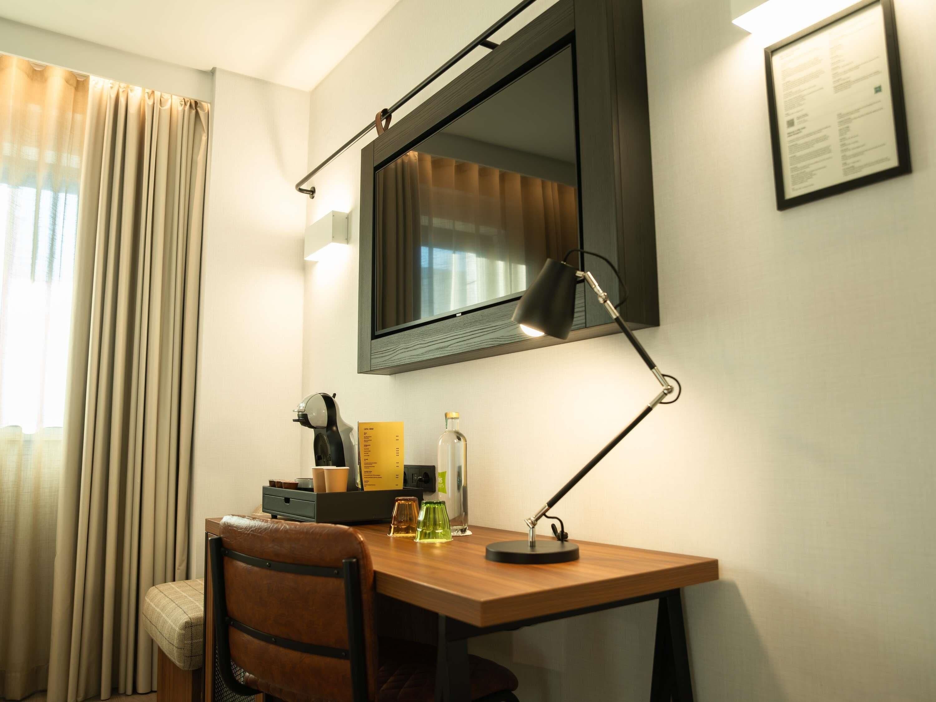 Habitación de hotel con escritorio, silla, lámpara y un espejo grande.
