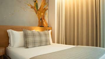 Une chambre d’hôtel avec un lit, une table de chevet, une lampe, un tableau au mur et une fenêtre avec des rideaux.