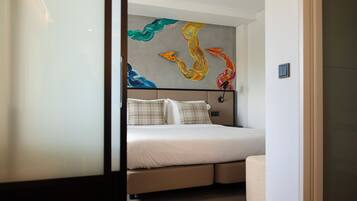 A modern hotel room with a bed, a headboard with a colorful abstract painting, and a small bedside table.