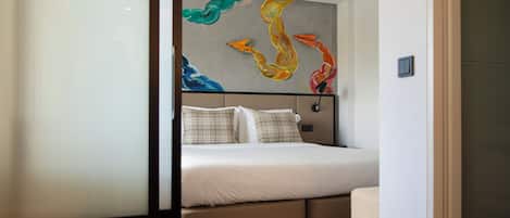 Una habitación de hotel moderna con una cama, un cabecero con un cuadro abstracto de colores y una mesita de noche pequeña.