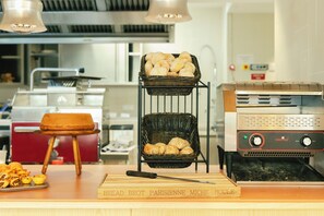 A bakery counter with bread and pastries, a bread slicer, and a display of bread baskets. - ibis Styles Lisboa Aeroporto (Loures)