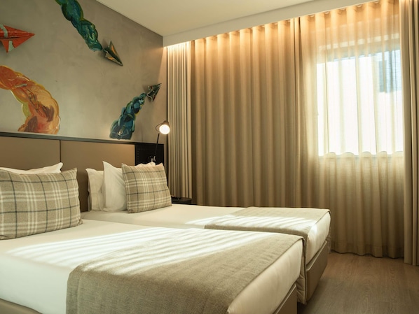 Habitación de hotel con dos camas, cabeceros, mesitas de noche, lámparas y un ventanal con cortinas.