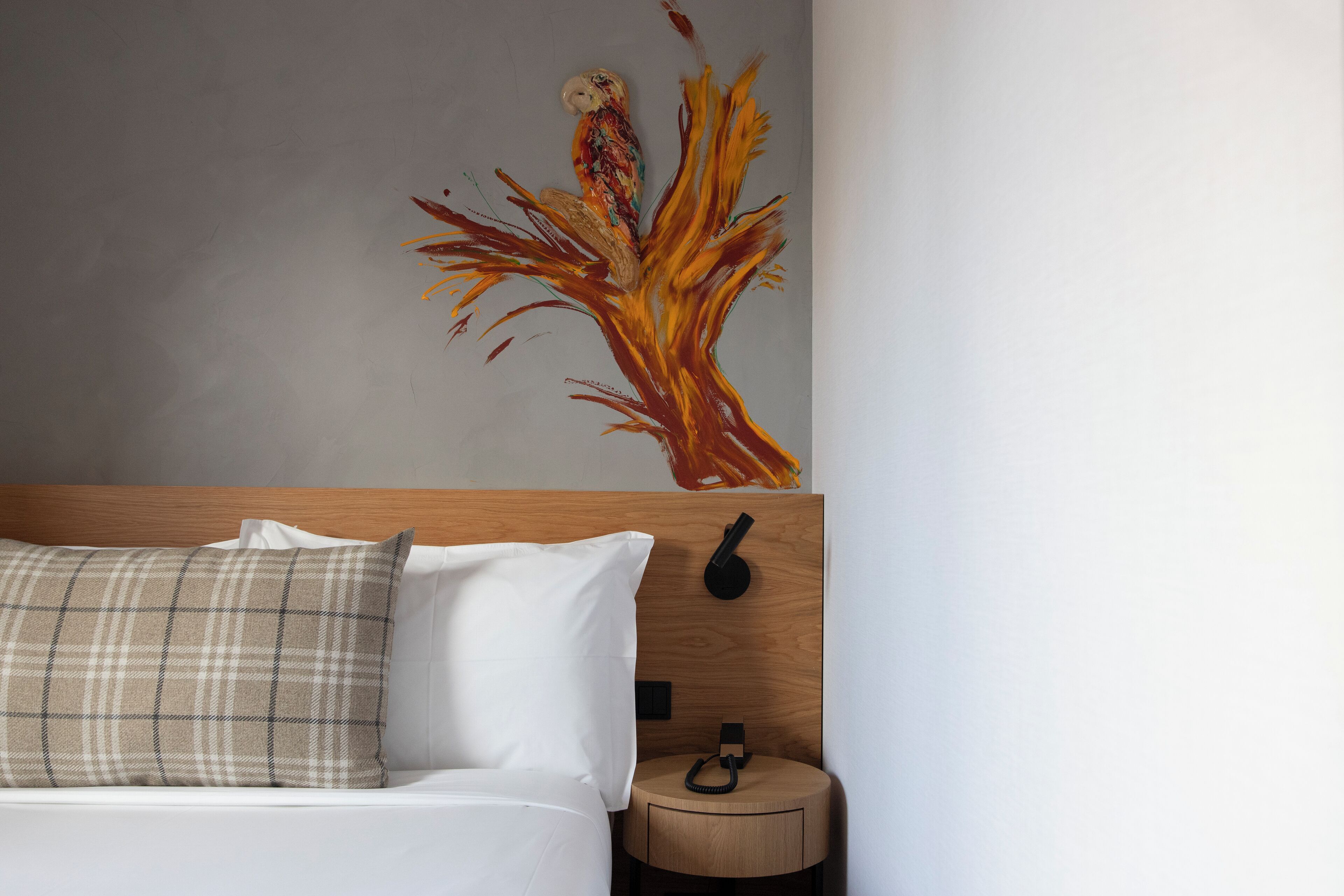 A bedroom with a bed, a nightstand, a wall-mounted telephone, and a painting of a tree.