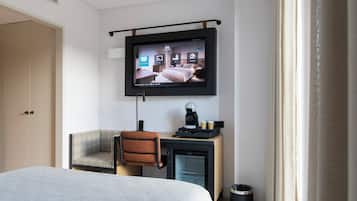 A hotel room with a bed, a desk with a chair, a television mounted on the wall, and a coffee machine.