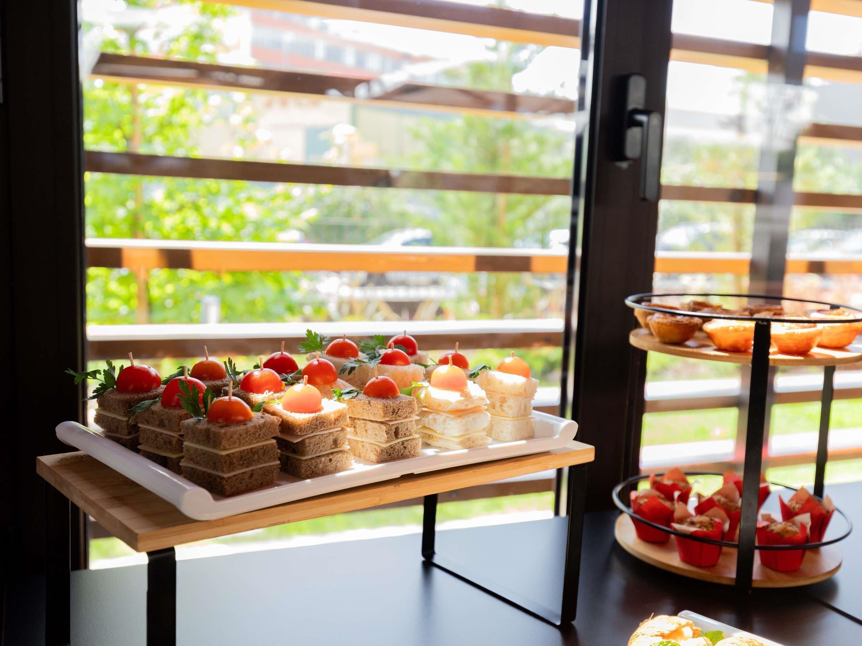 Una mesa de buffet con diversas opciones de comida, entre ellas sándwiches y pasteles, dispuestas sobre un soporte de madera.