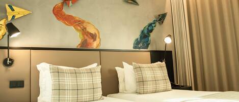 A hotel room with a bed, two bedside tables, a wall with abstract art, and a window with curtains.