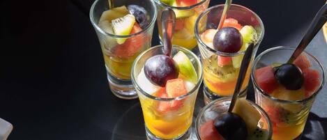 A series of clear glasses containing fruit and a liquid, possibly juice or water, with spoons.