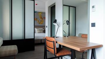 Una habitación de hotel moderna con una mesa de comedor de madera, una silla, una cama con cabecero y una obra de arte colgada en la pared.