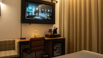 Quarto de hotel com cama, escrivaninha com cadeira, televisão na parede e minibar.
