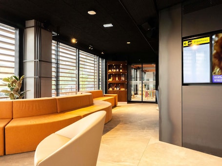 Ein modernes Interieur mit einer Sitzecke, einem Glastür-Eingang und einer Anzeigetafel für Abflüge.. ibis Styles Lisboa Aeroporto