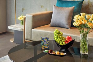 Una sala de estar moderna con un sofá, una mesa de centro con un frutero, un jarrón con flores y una tarjeta decorativa.