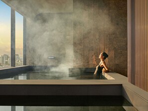 A modern indoor pool with a city view, steam rising, and a person relaxing. - Pullman Hai Phong Grand Hotel (Hai Phong)
