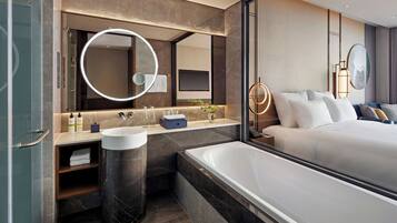 Une salle de bain d’hôtel moderne, dotée d’une grande baignoire, d’un miroir rond et d’un meuble-lavabo.