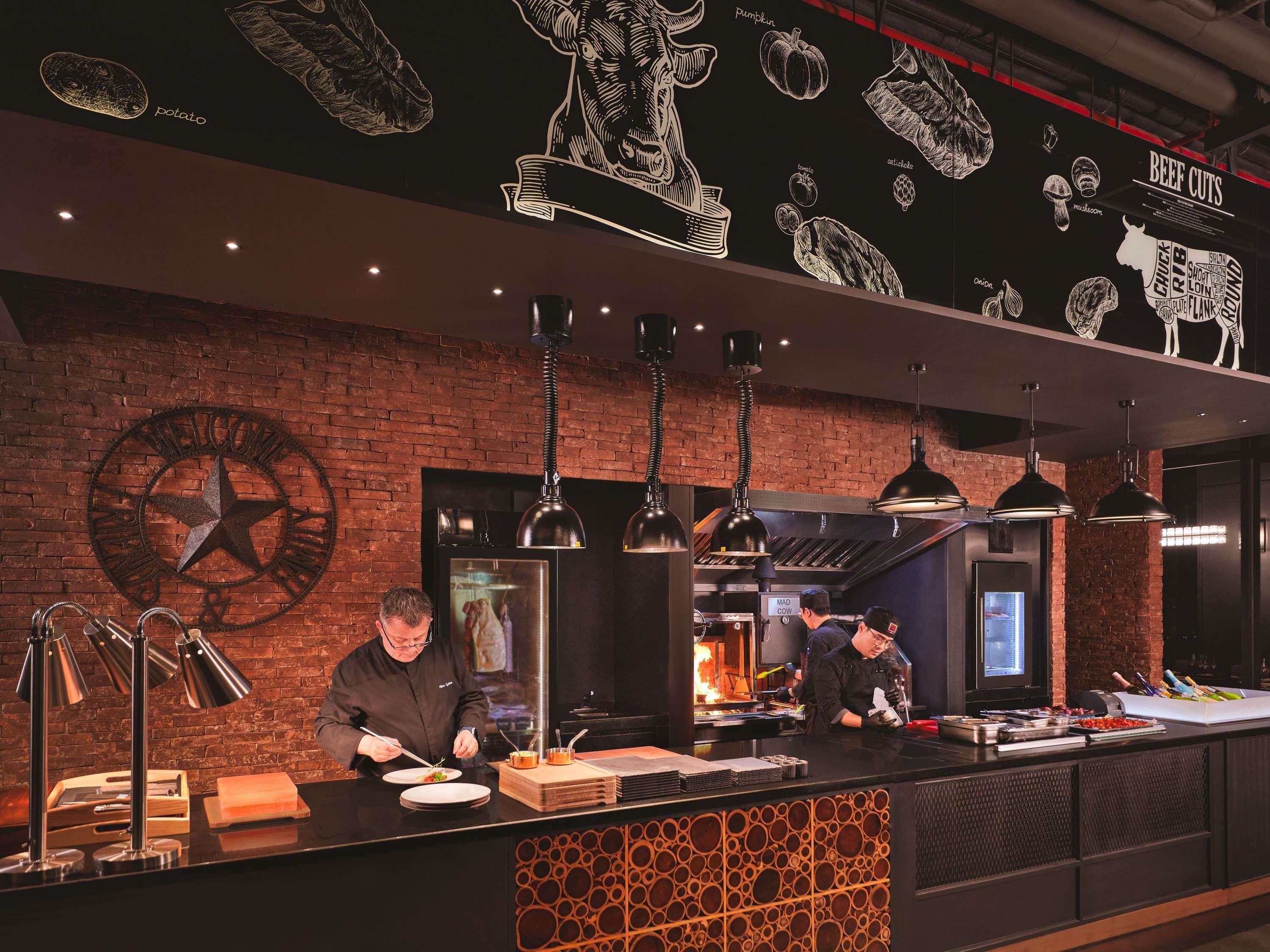 A restaurant interior with a brick wall, a clock, and a counter where chefs are preparing food.