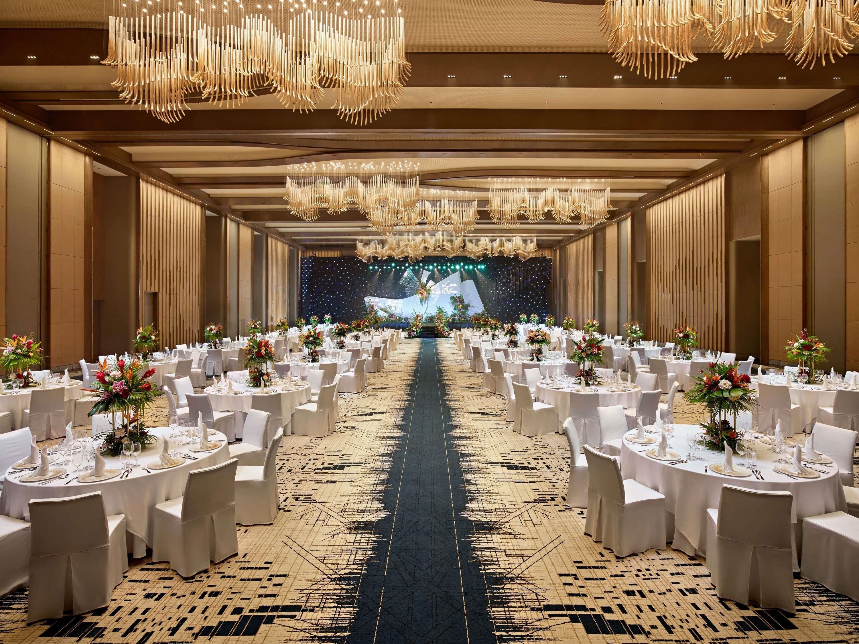 A banquet hall with round tables, white chairs, and chandeliers.