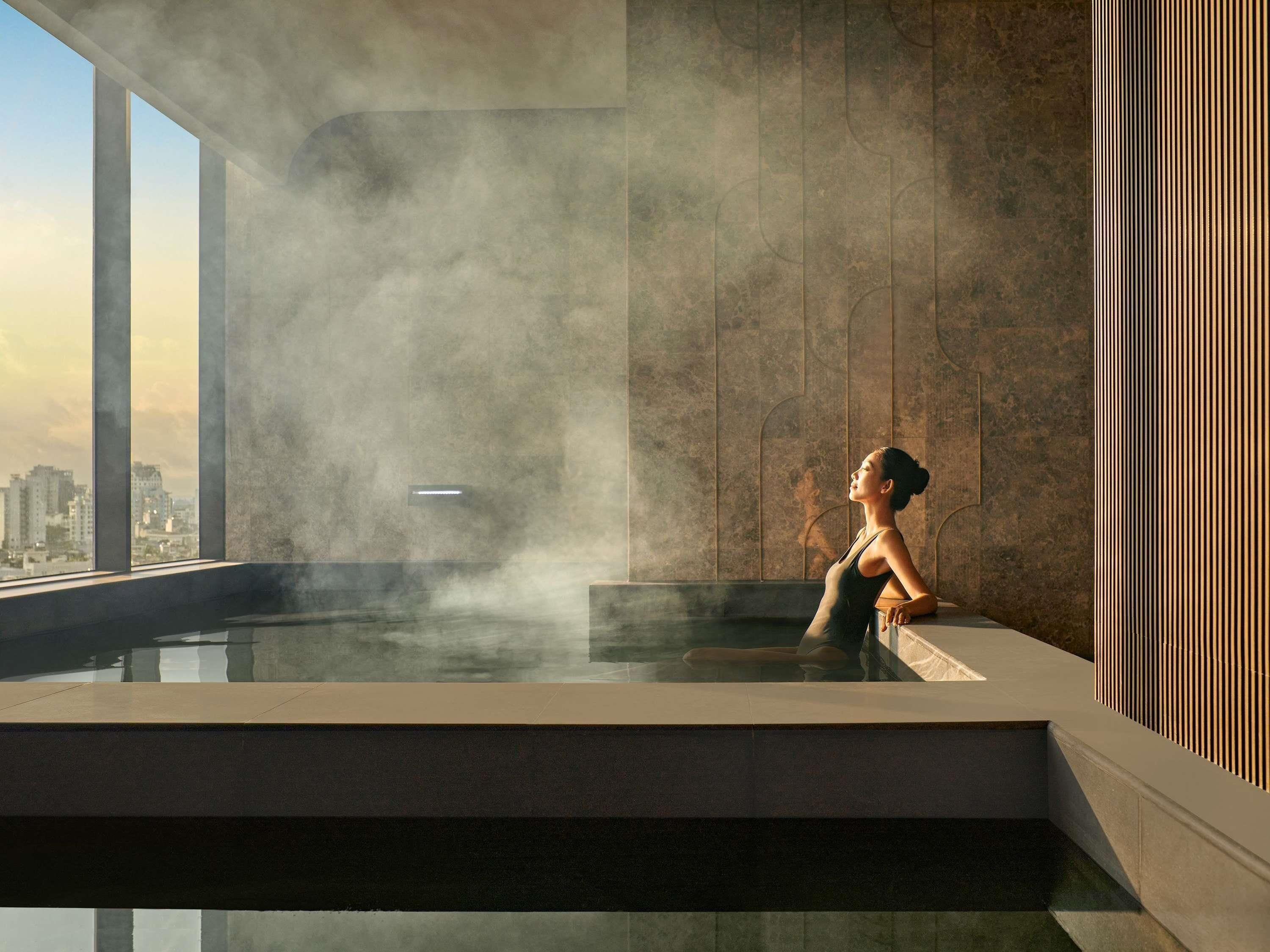 A modern indoor pool with a city view, steam rising, and a person relaxing.