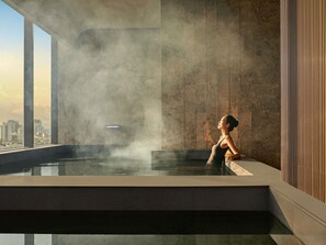 A modern indoor pool with a city view, steam rising, and a person relaxing. - Pullman Hai Phong Grand Hotel (Hai Phong)