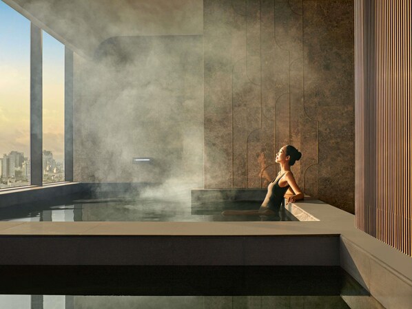 Piscina interior moderna con vista a la ciudad, vapor ascendente y una persona relajándose.