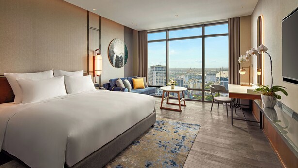 Una habitación de hotel moderna con una cama grande, un sofá, un escritorio con una silla y vistas a la ciudad.