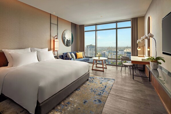 A modern hotel room with a large bed, a sofa, a desk with a chair, and a view of the city. - Pullman Hai Phong Grand Hotel (Hai Phong)