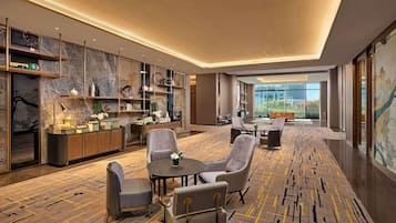 Een moderne hotel lobby met een zithoek, een receptiebalie en uitzicht op het omliggende landschap.