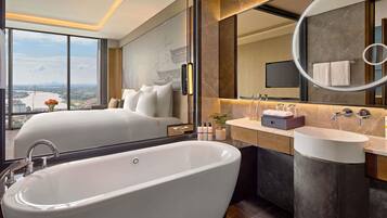 A modern hotel room with a large bathtub, a vanity with a mirror, and a bed with a city view.