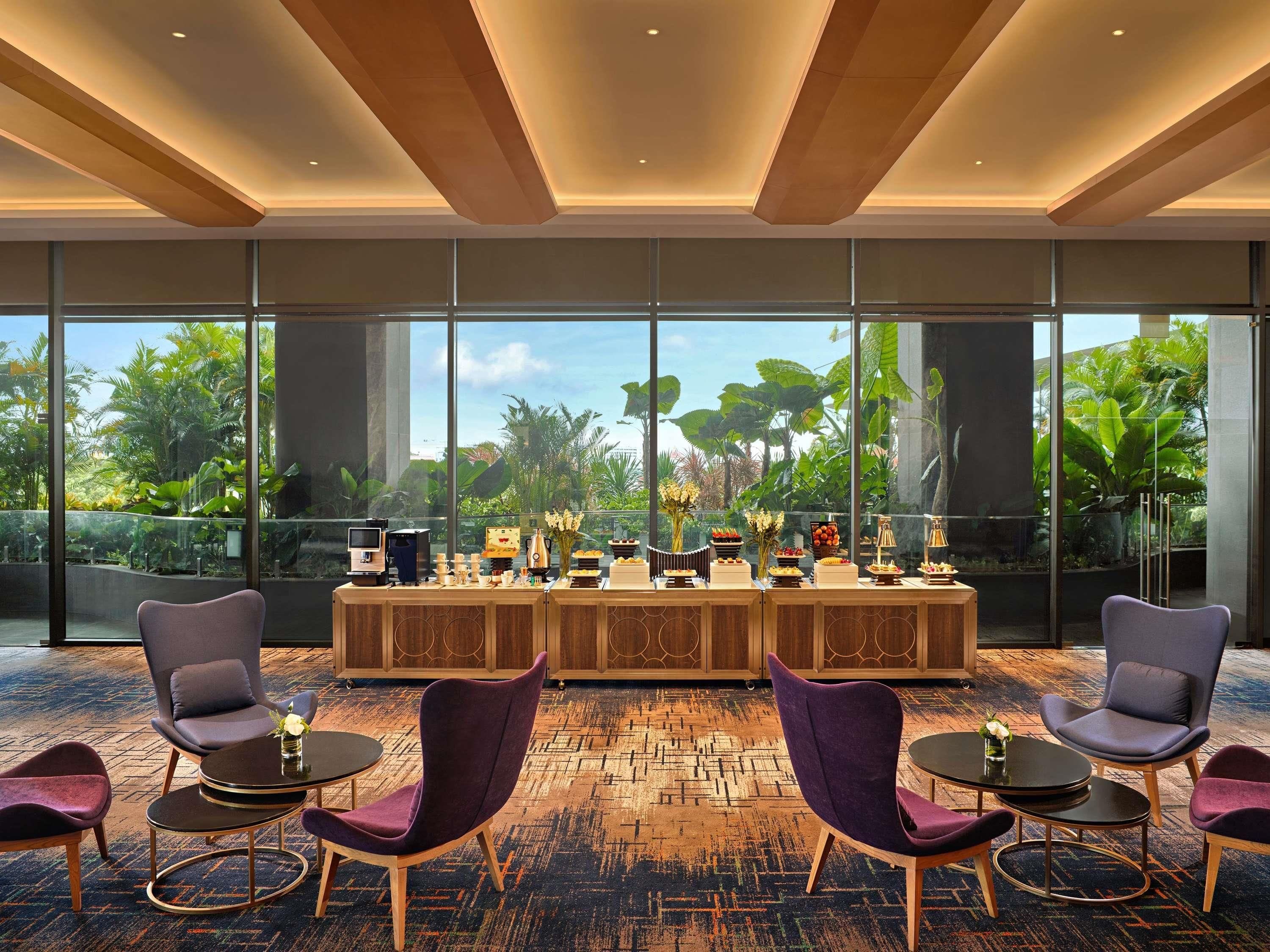 A modern hotel lobby with a large window view, a reception desk, purple chairs, and a patterned carpet.