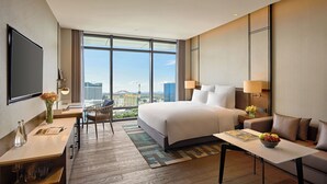 A modern hotel room with a large bed, a desk with a chair, a TV, and a view of the cityscape. - Pullman Hai Phong Grand Hotel (Hai Phong)