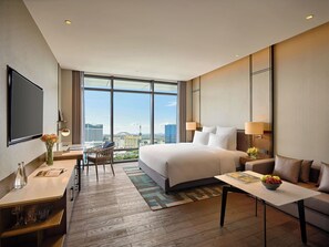 Una habitación de hotel moderna con una cama grande, un escritorio con una silla, un televisor y vistas a la ciudad.