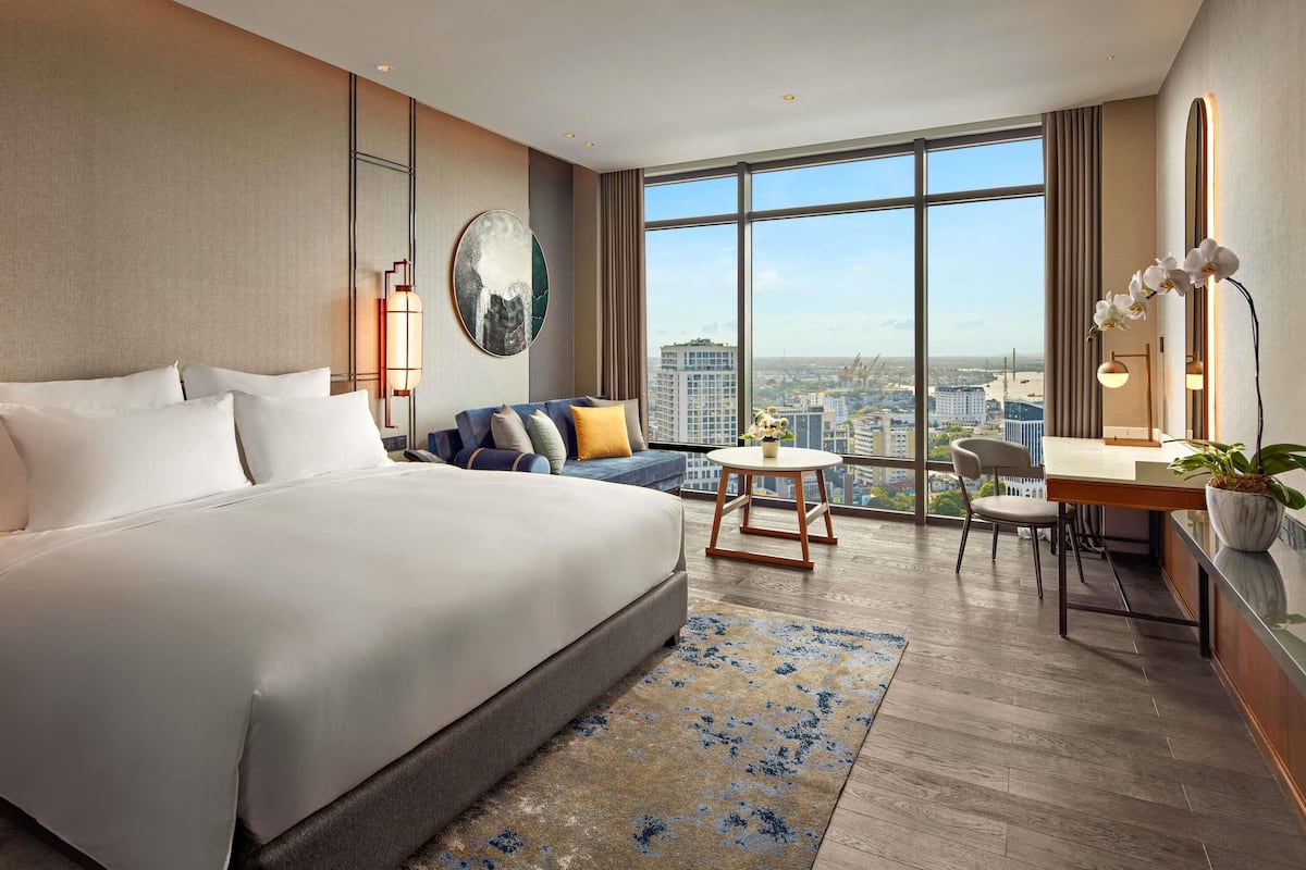 A hotel room with a large bed, a sofa, a desk, and a view of the city.