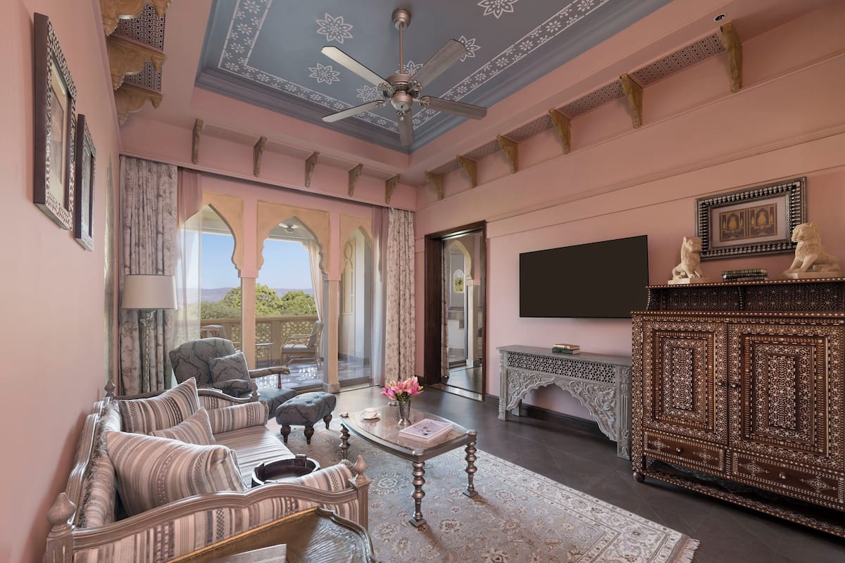 Quarto com sofá, poltronas, mesa de centro, televisão e um aparador decorativo.