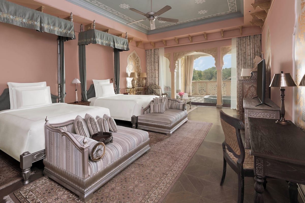 A spacious bedroom with two beds, a sofa, a desk, and a balcony with a view.