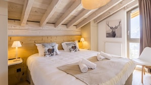 A wooden cabin-style bedroom with a large bed, two pillows with deer prints, a bedside lamp, and a framed deer head on the wall. - Wifi, sauna, terrace, balcony, parking, tv, ski locker, 80-95m², La Rosière (La Rosière Montvalezan)