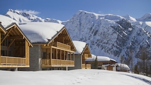 A chalet-style building with a wooden facade and stone foundation, surrounded by snow-covered mountains. - Wifi, sauna, terrace, balcony, parking, tv, ski locker, 80-95m², La Rosière (La Rosière Montvalezan)