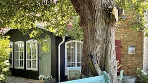 Une structure rustique en bois, avec un banc, un grand arbre et un mur de briques.