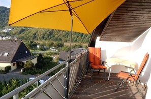 Un balcon avec un parasol jaune, une chaise et une table.
