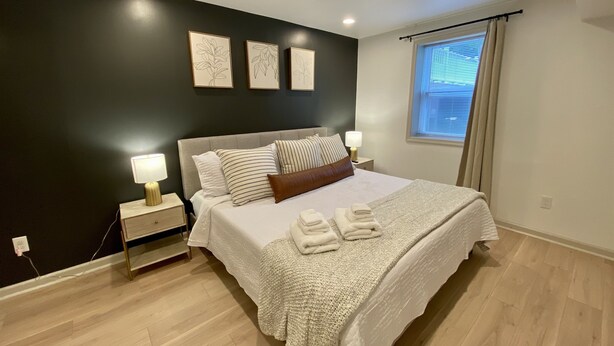 A bedroom with a bed, bedside lamps, a window with curtains, and artwork on the wall.