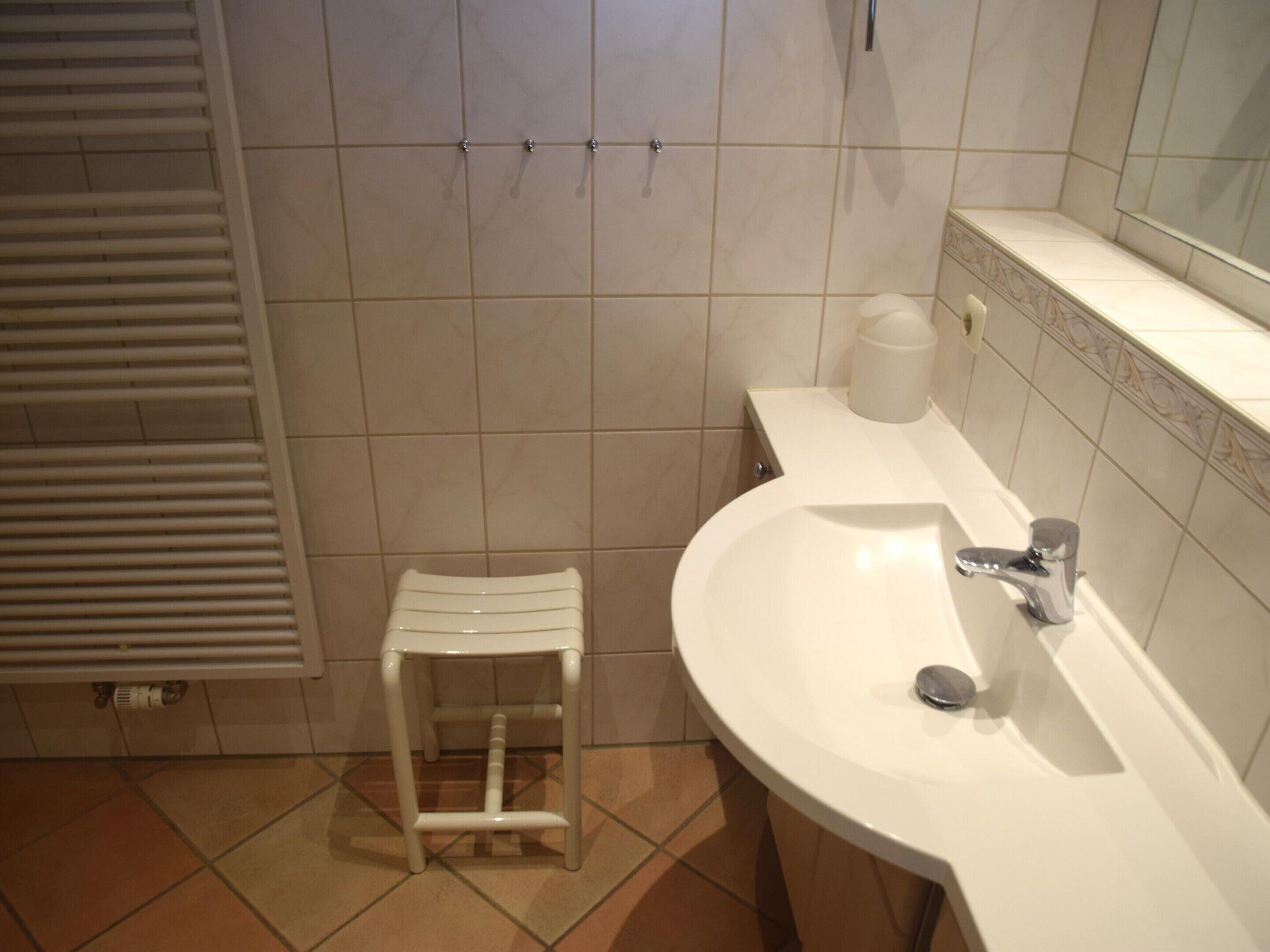 A bathroom with a white sink, a mirror, and a small stool.