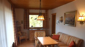 A cozy room with a wooden table, striped sofa, and a window with curtains. - Comfort With Garden Views (Fuessen)