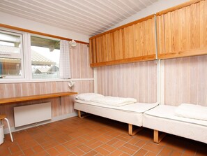 A room with two beds, wooden cabinets, a window with curtains, a small table, and a radiator. - 6 Person Holiday Home on a Holiday Park in Hanstholm (Hanstholm)
