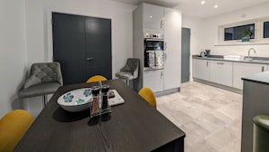 Una cocina moderna con comedor, que incluye una mesa de madera oscura, dos sillas grises tapizadas, una puerta negra y un horno empotrado.