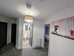 Un couloir orné d’un lustre, d’un radiateur et d’un tableau accroché au mur.