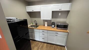 A compact kitchen with white cabinets, a stainless steel sink, a microwave, and a coffee maker.