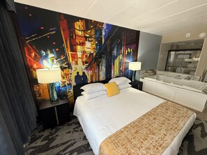 Habitación de hotel con una cama grande, dos lámparas de noche, un baño moderno y un cuadro abstracto y llamativo en la pared.