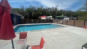 A swimming pool with a fenced area, lounge chairs, and a table.