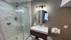 A modern bathroom with a glass shower, marble tiles, a round mirror, and a vanity with a sink and towel rack.