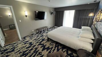Une chambre d’hôtel avec un grand lit, un téléviseur à écran plat fixé au mur, un banc et une petite table avec une lampe.