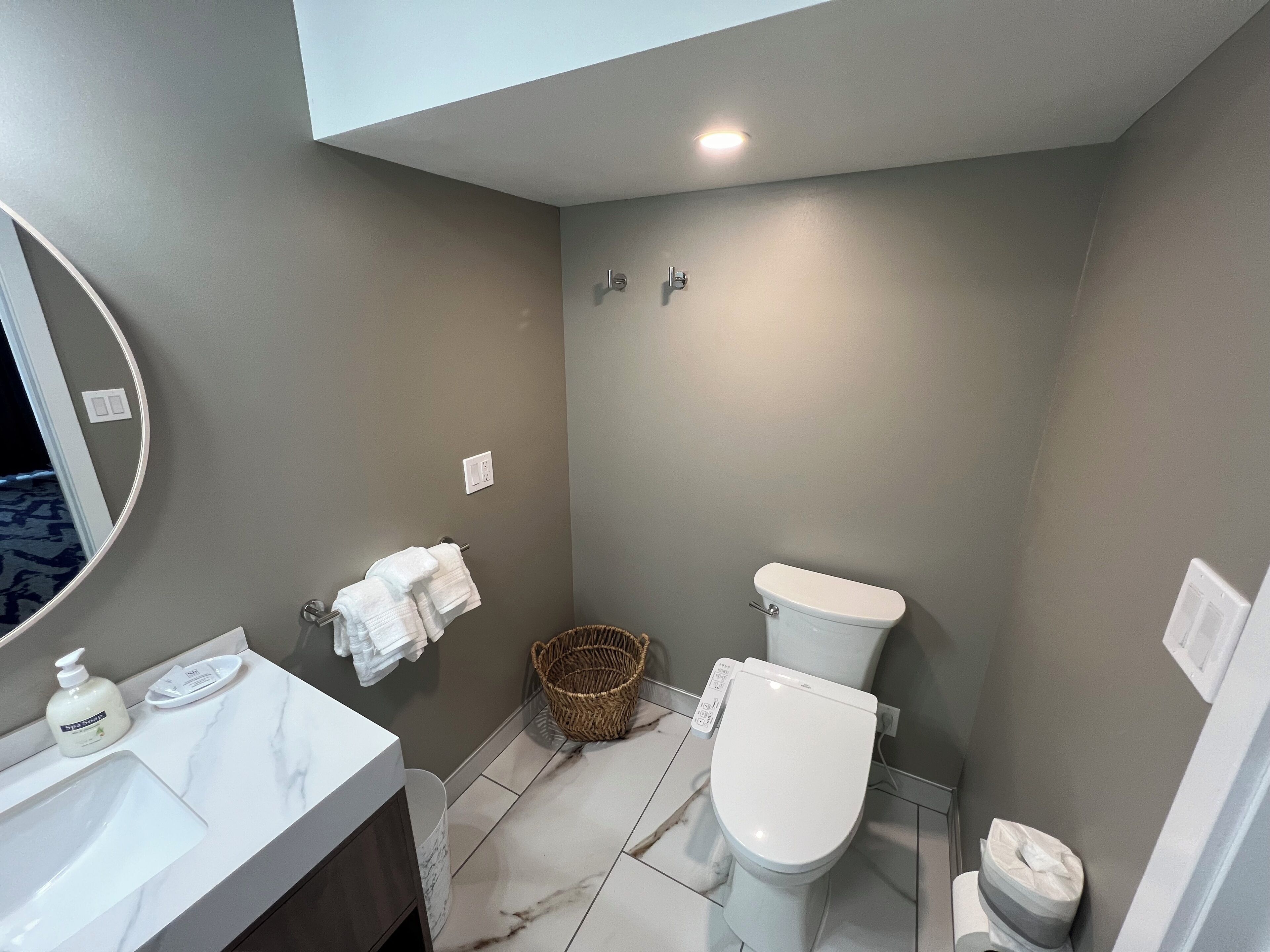 Een badkamer met een wit wastafel, toilet, spiegel en mand.